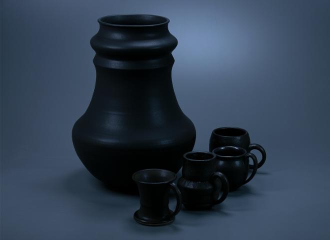 A matte black group of pots. One larger vase surrounded by four smaller mugs on it’s right side.