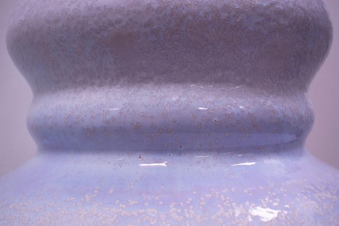 Close up of the crystalline glaze of a tall vase. The glaze is a semi-glossy white with a subtle blue/purple hue and is covered with clusters of crystals.