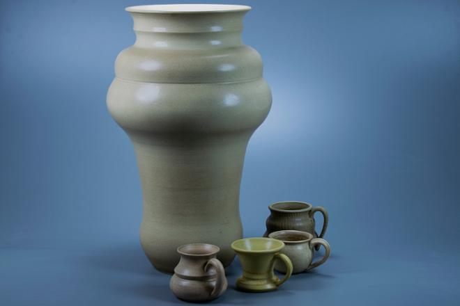 A group of semi-matte tan glazed pots. A taller tan vase stands with four smaller tan mugs surrounding it's right side.