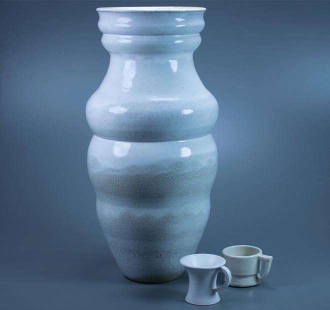 A group of semi-glossy and matte white pots. A tall semi glossy vase is accompanied by two mugs at it's right side. One mug is matte white and the other is a glossy white snowflake crackle glaze.
