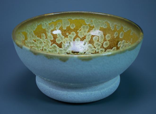 A cereal bowl sized bowl with a sandpaper textured white glazed on the outside and a yellow and gold crystalline glazes on the inside.