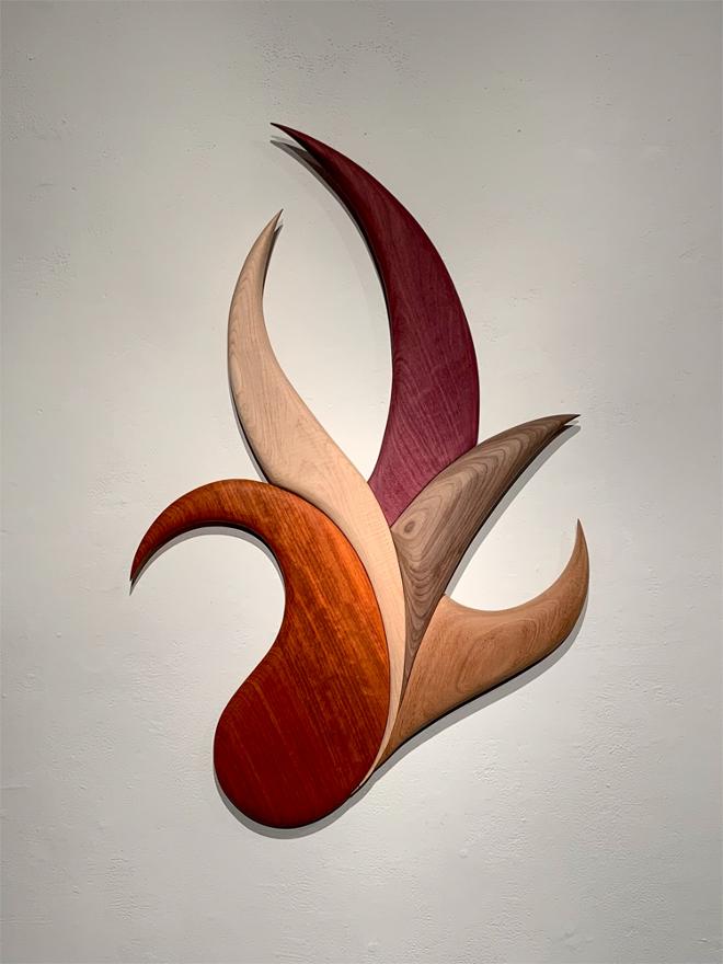 Five different colors of wood cut in various curves and fit together to form an abstract wall piece.
