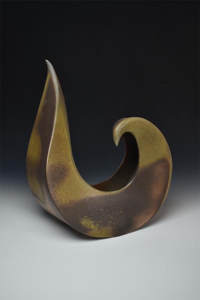 A slab-built, sculptural vessel in the form of an abstract, curling wave.