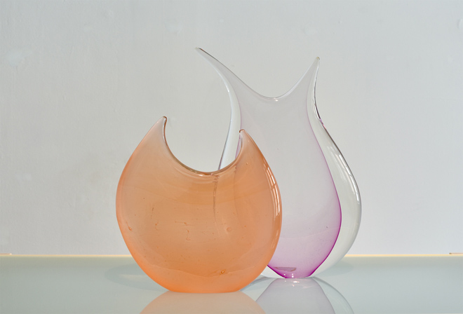 Two flattened glass sculptures, one is peach-colored and the other is fuchsia.