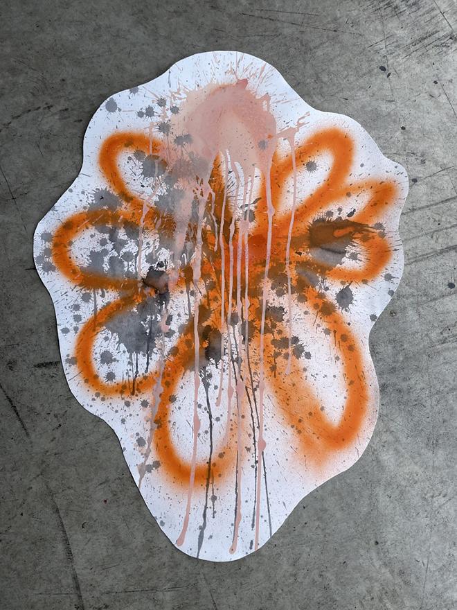 The painting is done on a white background, displaying several tiny diluted ink splatters. A bright orange flower has been spray painted largely on the page and the edges of the paper have been cut to mimic the shape. A light pink spot has been sprayed in paint at the top of the page and bled down the length of the paper leaving multiple trails.  