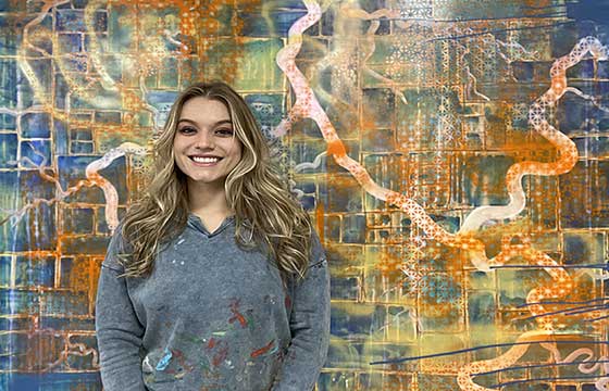 Jackie standing in front of highly patterned painting, smiling, hair down