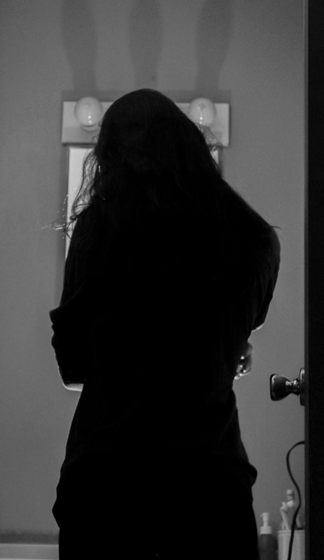 A figure looking into a mirror with dramatic lighting and shadows