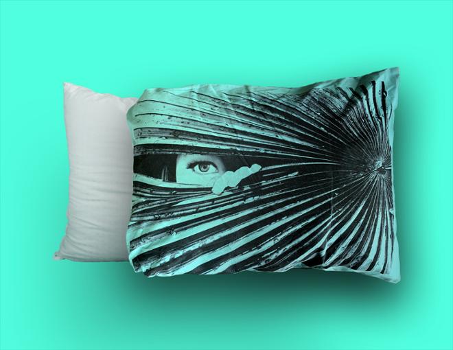 Eyes and hand peering through a fern, printed on a teal pillow case. 