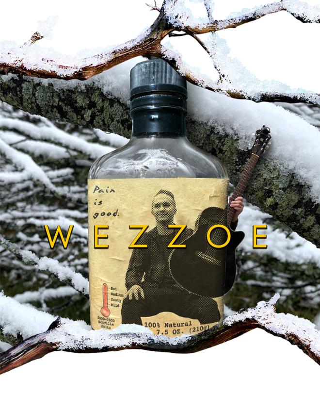Hot sauce bottle in the snow, a smiling guitar player is featured on the bottle’s label. 
