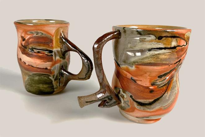 Two ceramic mugs with striking orange flashing and contrasting glossy grey glaze made from baking soda. The handles are made from a darker clay than the porcelain cup and are inspired by line drawings of my long-time friend (Eleda). 