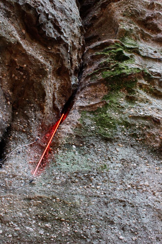 A straight red neon line traces the negative space along a wall of rock. 