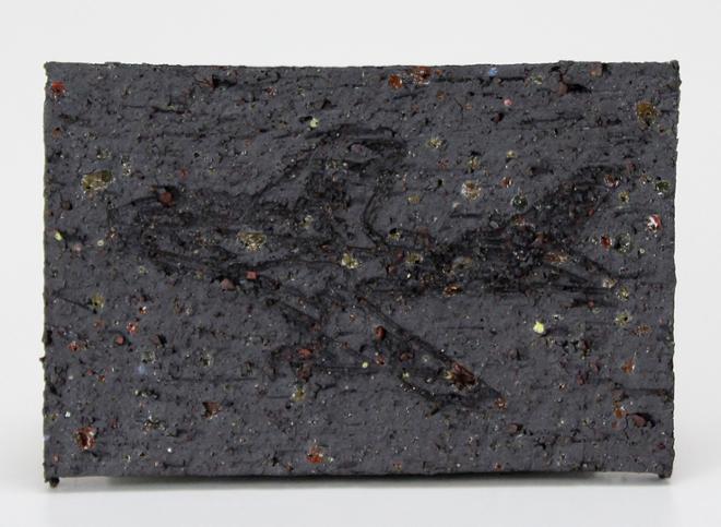 A black ceramic tile with flashes of color throughout. Etched into the surface is an image of a plane.