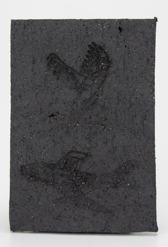 A black ceramic tile with an image of a bird above an image of a plane etched into the surface.