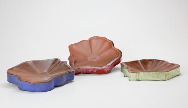 A set of three plates that are soda fired. Red to dark brown gradient on the interior of the plates. Lined with a red, blue, and yellow glaze on the exterior. 