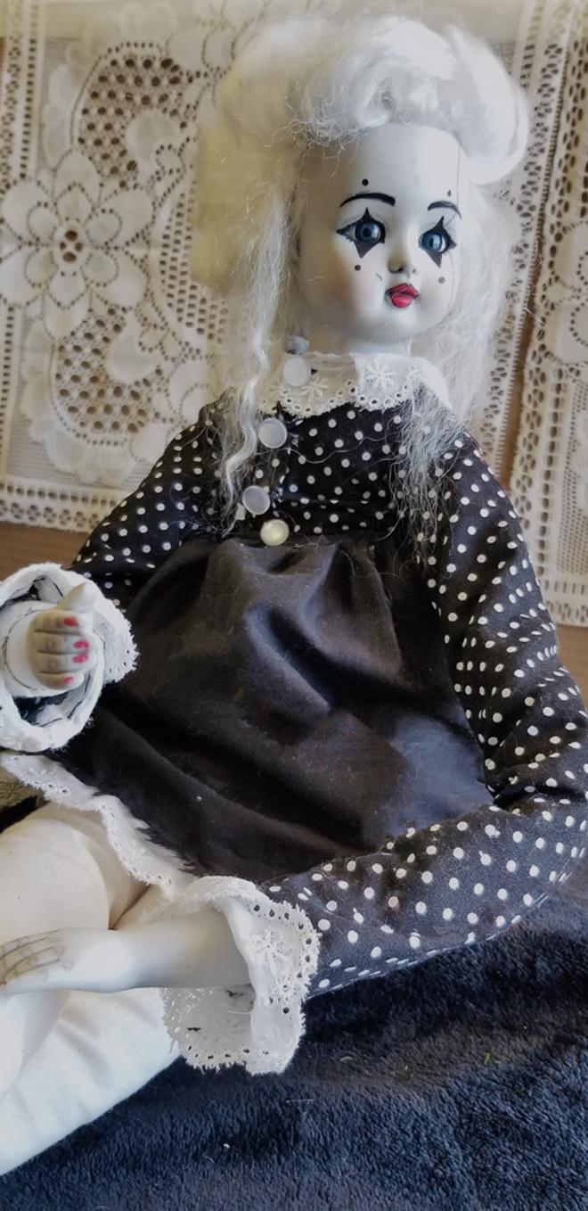 A porcelain doll sculpture with extended limbs, handmade clothes, and a painted face.