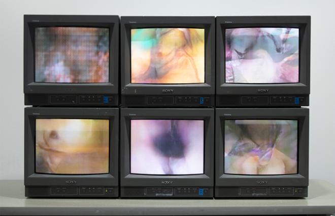 6 CRT televisions stacked as 3 horizontal and 2 vertical each playing different videos as seen from straight on 