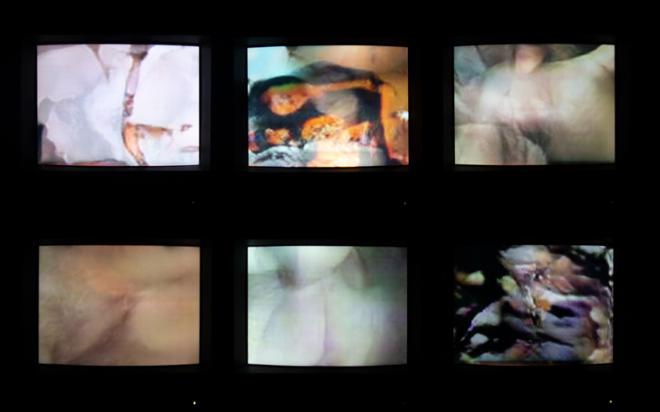 6 CRT televisions stacked as 3 horizontal and 2 vertical each playing different videos seen from straight on and in the dark