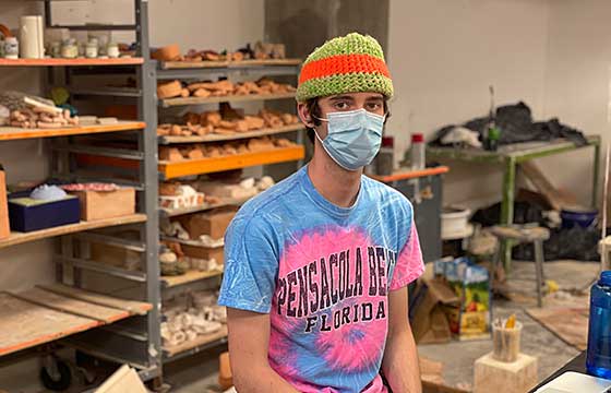 Colin sitting in studio with orange and green beanie, mask and blue and pink tie die shirt