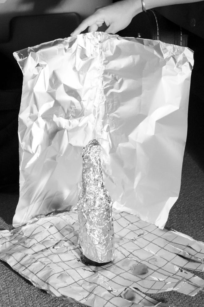 Photograph of a  glass bottle covered with aluminum, placed inside of a constructed scene held up by a hand.