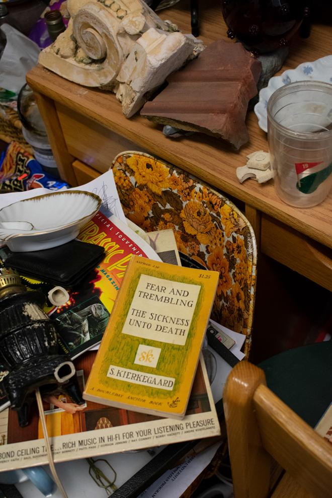 Photograph of a cluttered group of books, bowls, vinyl albums, and miscellaneous objects on a plastic chair, on top of the pile is the book “Fear and Trembling: The Sickness Unto Death” by Søren Kierkegaard.