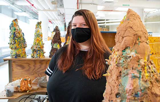 Bri standing in black mask beside a life sized ceramic sculpture