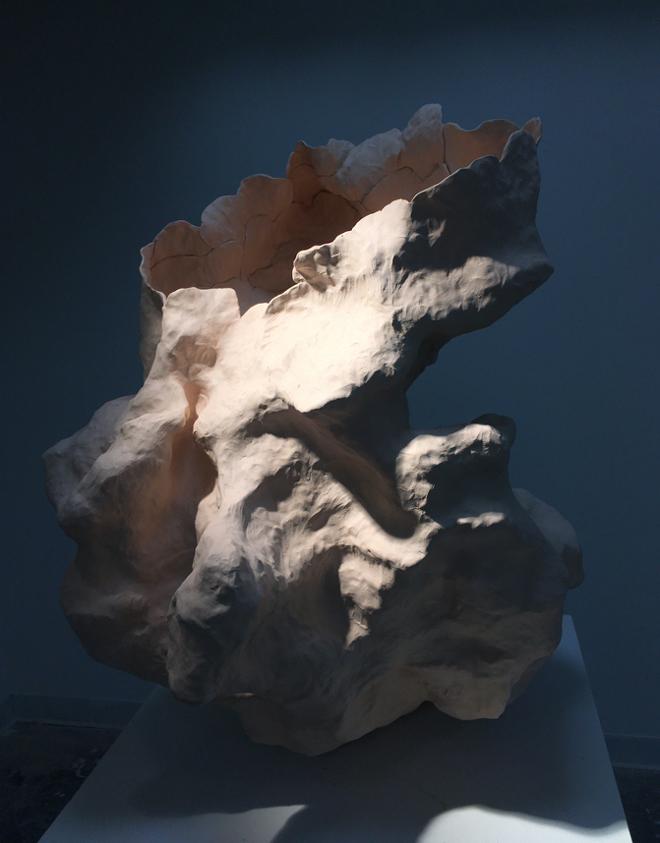 A bare breathing ceramic mass with very thin, delicate walls is displayed on a pedestal with dramatic lighting to emphasize the form’s concave and swelling skin. 