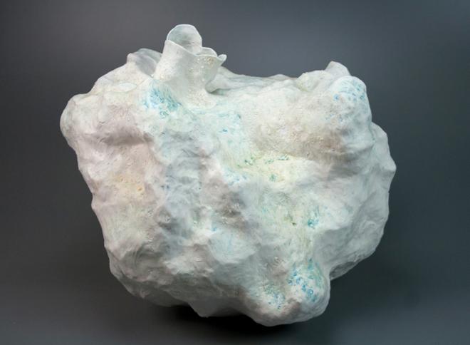 A cloudlike and glowy ceramic vessel is shown with an iridescent white surface that flakes in some areas and shines blue and bronze in others, reminiscent of a Greek god. 