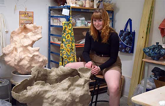 Sarah sitting on stool in her studio behind sculpture in progress