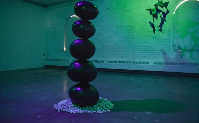 Front view of black ceramic spheres with green and purple lighting. In the back is Finding Peace, a steel structure with jagged triangles.  