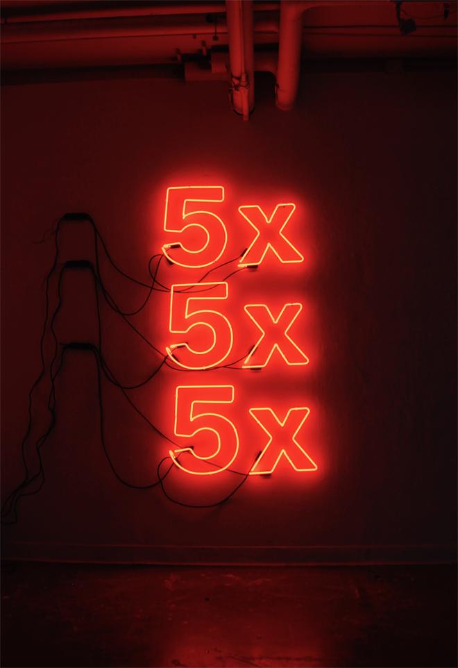A vertical wall installation of three orange neon signs spelling, “5x” stacked on top of each other.