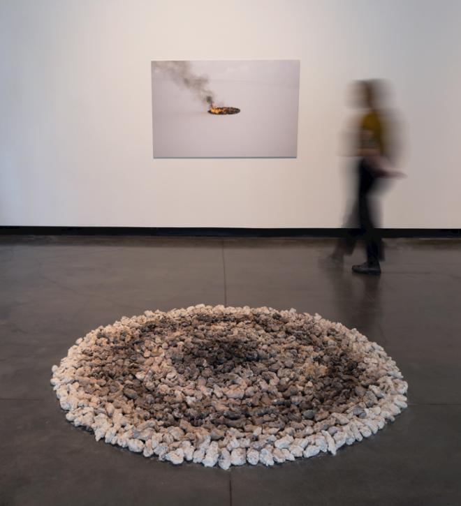 A large Photography mounted on the wall, a circular sculpture made of hand size chunk of clay Display in a gradient color pattern. A person looks at the picture