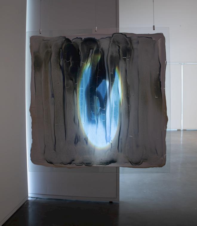 Light sensitive clay is reacting to a projecting video and changing colors over time. Large piece of glass suspended