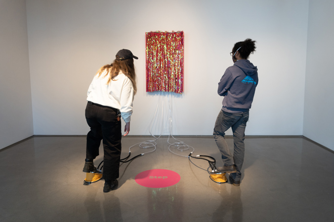 two people interacting with foot mechanism on floor that connects to a colorful wall piece