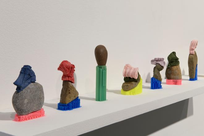 A narrow white shelf holds an array of colorful rock, printed plastic, and porcelain sculptures. 