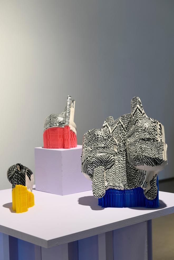 A detail shot of three black and white sculptures balanced on colorful plastic stands. 