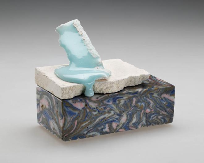 a rectangular object with blue, pink, brown, and white marbling. A white slab sits on top with light blue glaze dripping down.