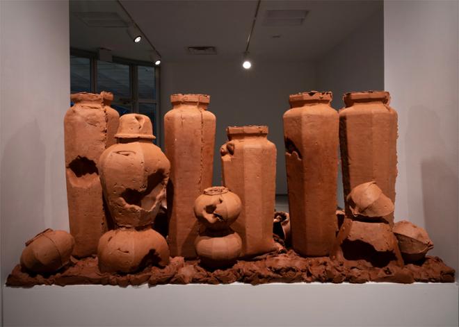 a 20 inch tall plinth packed with 38’’ tall urn forms, and an ecosystem of smaller pots, clay chunks, and larger than life seed pods.  The plinth and it’s installation are wedged between a column and the wall, totally blocking the walkway for the space