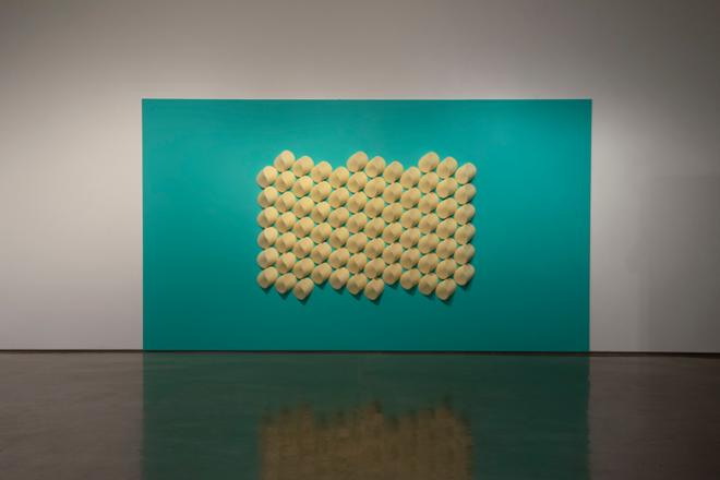 a large, yellow tile piece on a teal wall. The tiles are ovular in shape and arranged in a geometric pattern