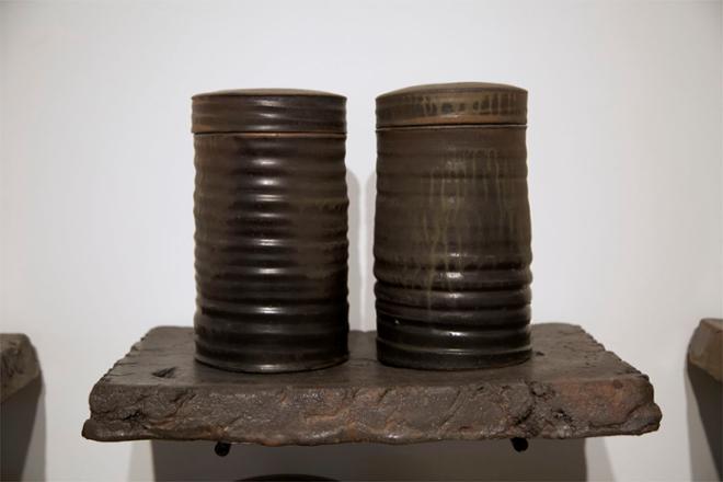 One dark ceramic shelf comes off the wall, with two jars sitting on it. The shelf is 20” wide and 2” thick. The jars are vertical cylinders about 12” high with obvious throwing lines from a potter’s wheel. They are a pair, with a similar dark matte variegated glaze which is made up primarily of a local shale from around Alfred. 
