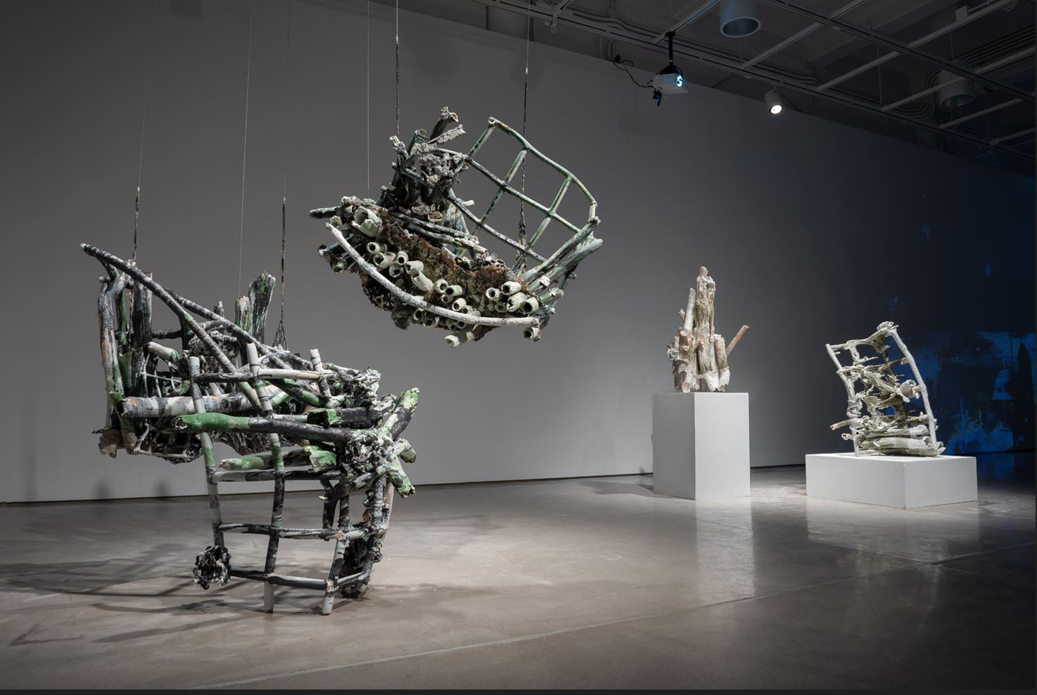 Installation image of a grouping of three large-scale grid sculptures, two of which are suspended by latex-coated nets. In the background, two more sculptures are visible on pedestals. 