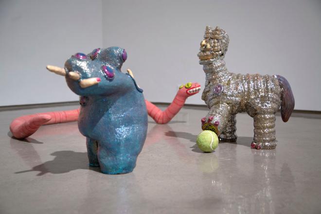 Three animal-like ceramic sculptures playing with a ball on the floor.  