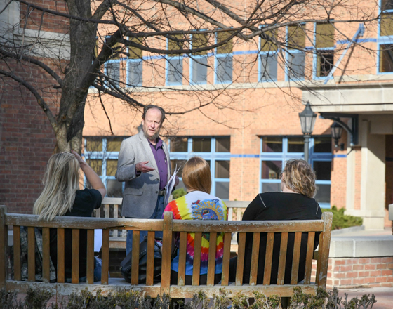 Students outside with a professor at park benches learning