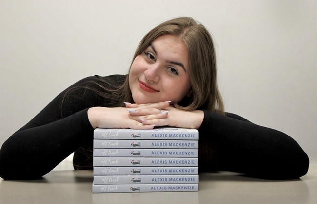 A photo of Alexis Izyk with multiple copies of her novel Off Track