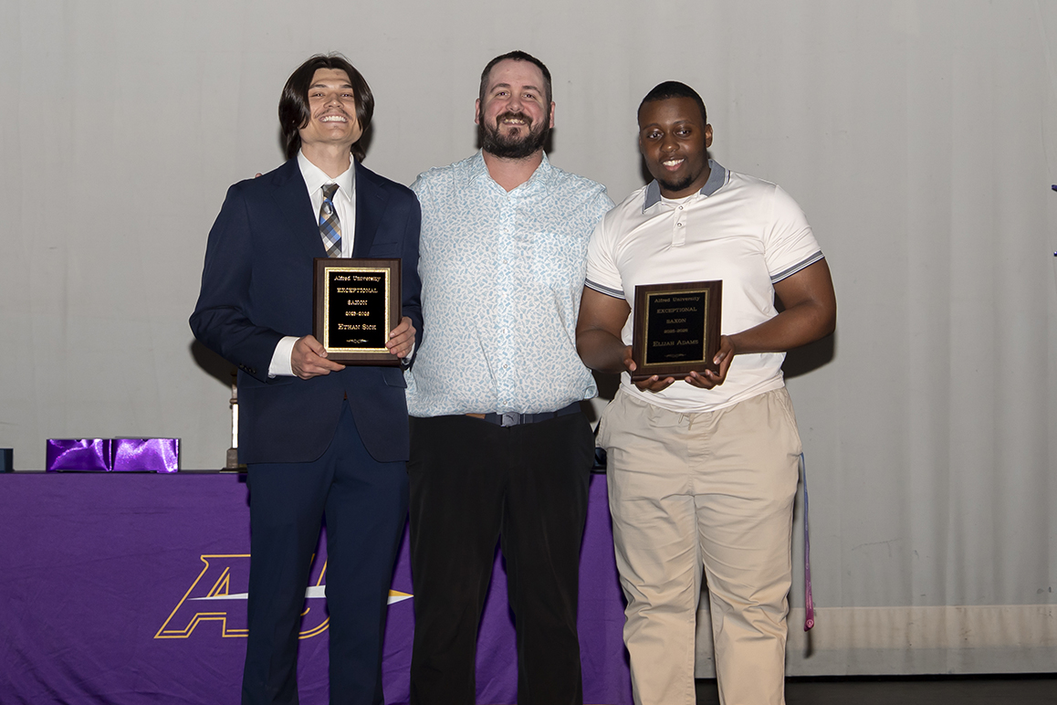 A photo of two Alfred University students and a staff member smiling and holding an award