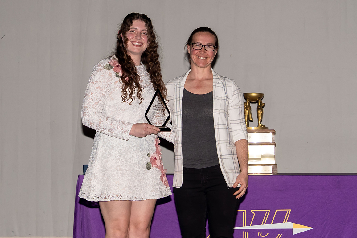 A photo of an Alfred University student and a staff member smiling and holding an award