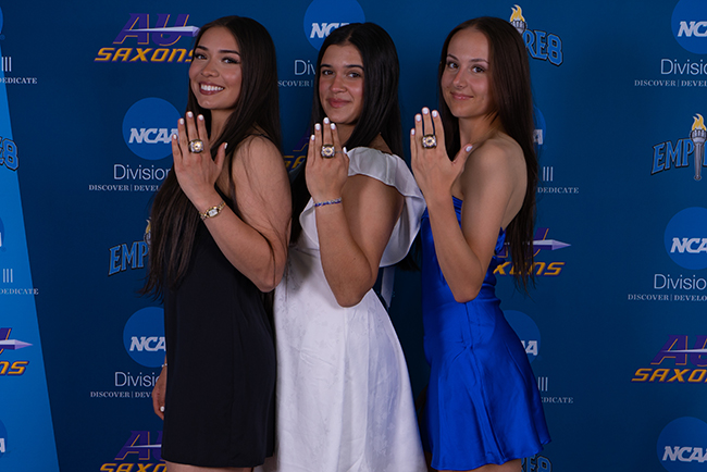 A photo of three female Alfred University student-athletes smiling and holding up championship rings