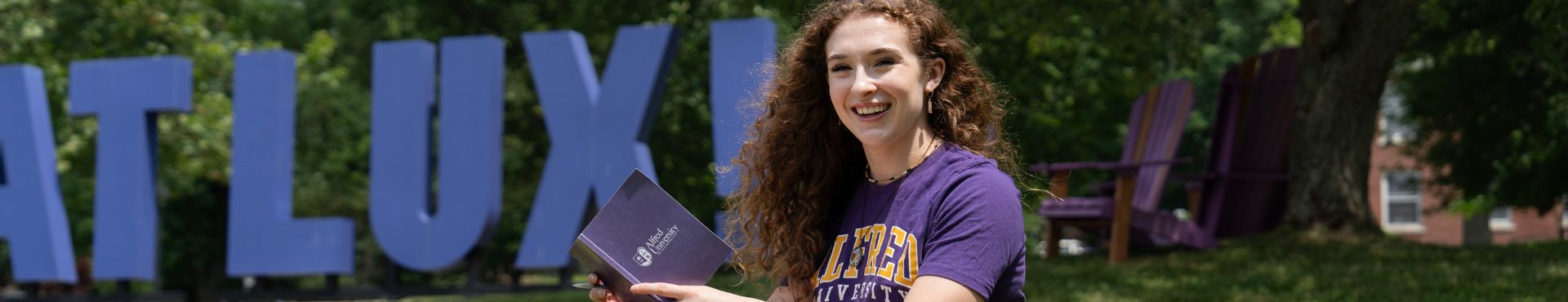 A female shown next to a large purple sign on a college campus that says Fiat Lux!