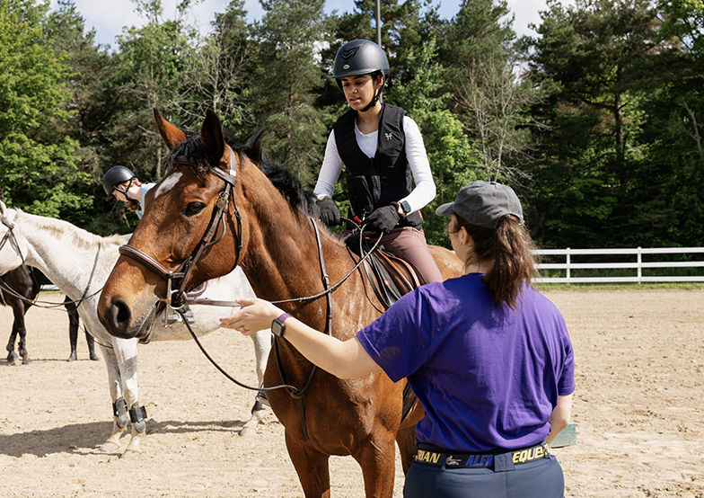 A photo of an Alfred University equestrian coach teaching a high school student how to ride a horse