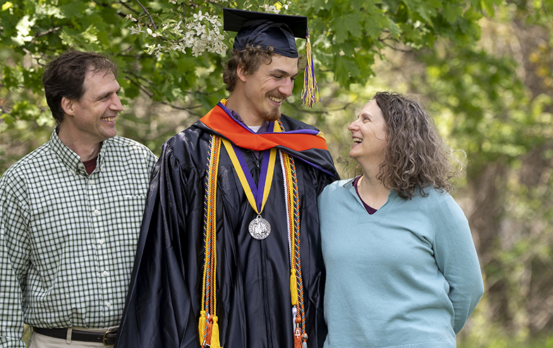 A photo of two Alfred University alumni standing with their young family graduate
