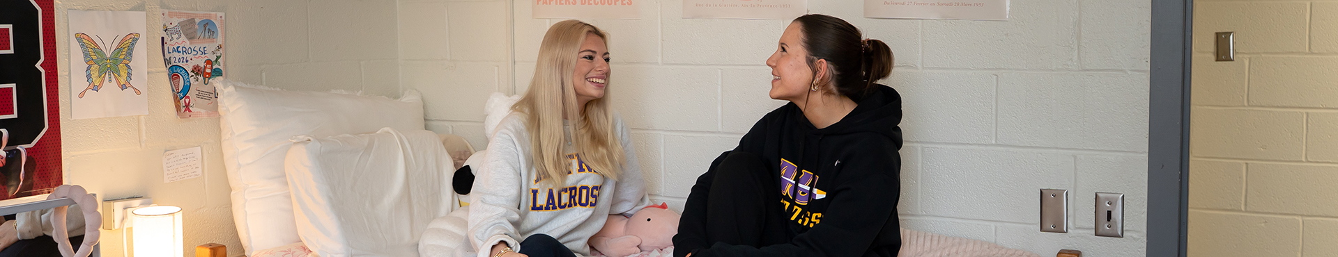 A photo of two Alfred University students sitting on a bed in a dorm room